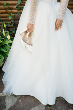 Bride in tulle wedding dress holding pair of white shoes