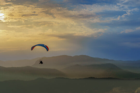 Paramotor Flying Over Mountain Range at Sunset.