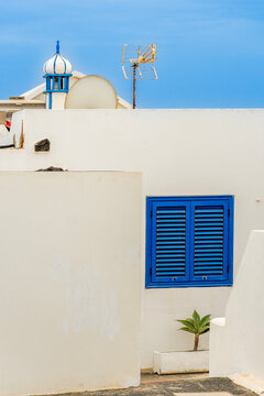 White coastal facade with blue shutters and palm tree