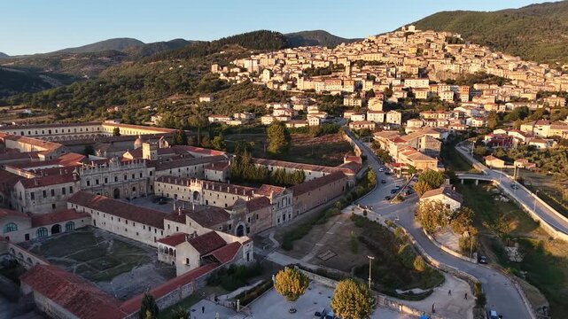Aerial view of the Carthusian monastery of Padula and the houses of the old village on the hillside at sunset, Campania, Italy