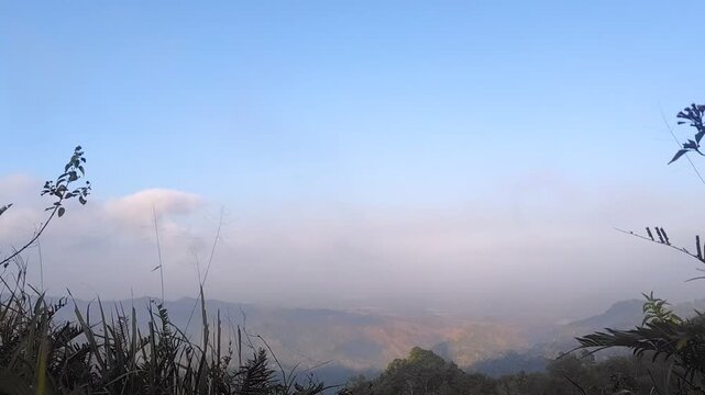 Clouds and morning mist moving across a hazy valley under blue sky, view from Menoreh Hills, Java, Indonesia, scenic mountain landscape in the fog