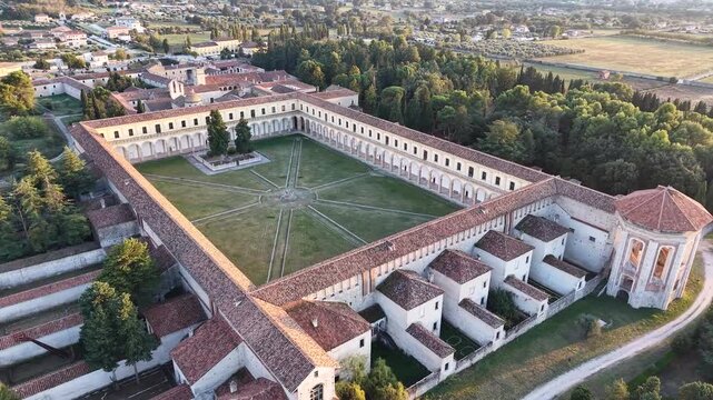 Aerial view of the Great Cloister of the Carthusian monastery of Padula surrounded by cypress trees at sunset, Campania, Italy
