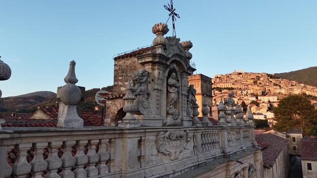 Baroque balustrade and statues of the Certosa di Padula with the hilltop village in the background at sunset, Campania, Italy