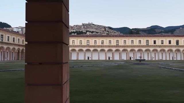 Arcades of the Great Cloister of the Certosa di Padula with the hilltop village of Padula rising behind, Salerno, Campania, Italy