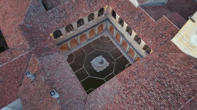 Top down aerial view of the fountain in the cloister of the Certosa di Padula surrounded by tiled roofs, Salerno, Campania, Italy