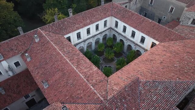 Aerial view of an arcaded cloister courtyard with trees and terracotta rooftops at the Certosa di San Lorenzo in Padula, Salerno, Italy