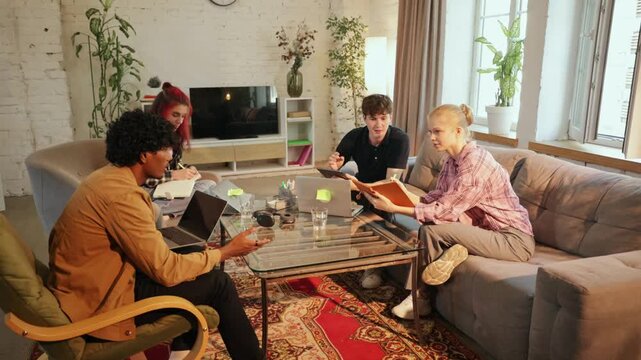 Four remote coworkers compare tablet and laptop content in apartment with collaborative interest. Device collaboration, project review, flexible work concept
