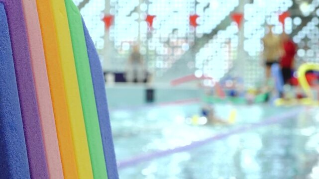 Bright multicolored foam pool noodles frame an indoor swimming pool, with sparkling water, colorful equipment, and decorative lights creating a playful atmosphere and copy space.