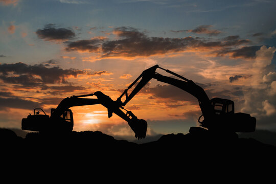 Two  Crawler excavators silhouette are digging the soil in the construction site on   sunset  clouds  sky background .