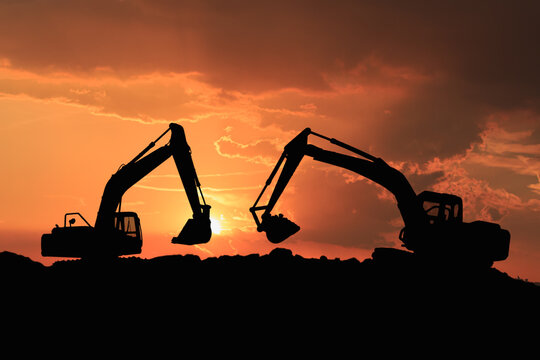 Two  Crawler excavators silhouette are digging the soil in the construction site on   sunset  clouds  sky background .