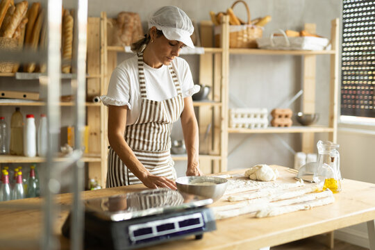 Female baker prepares raw yeast dough in bakery, forming it into long sausages to be cut into pieces for baking buns