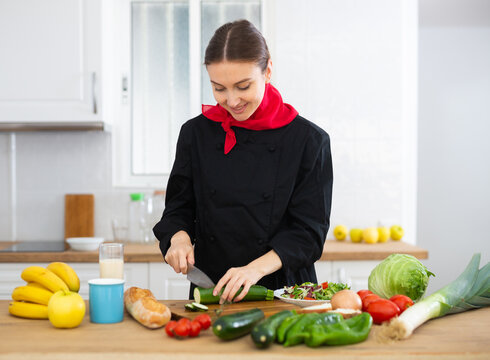 Female cook in black uniform chopping vegetables in kitchen