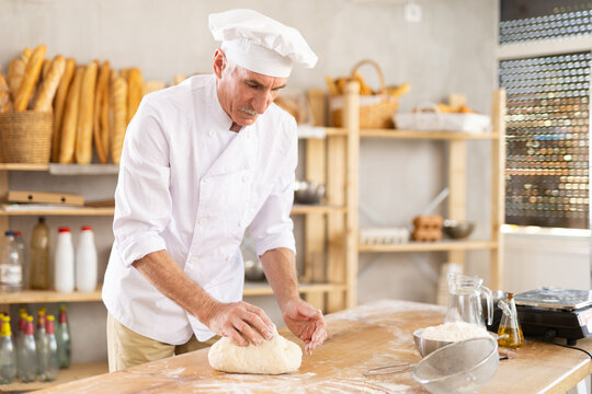 Elderly man kneads dough in bakery