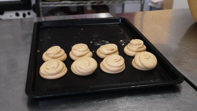 High angle view of neatly arranged spiral swirls of icing on a black baking sheet ready for baking in an artisan bakery kitchen. Concept for commercial pastry prep, batch baking