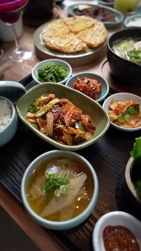 Vertical 4K footage of Korean meal set with bulgogi beef white rice soup kimchi pancake and side dishes banchan on wooden table.