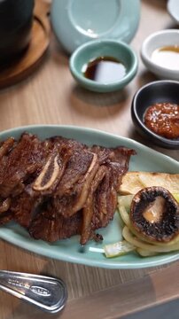 Close-up vertical 4K footage of delicious grilled beef short ribs galbi kalbi barbecue on blue plate with mushroom onion and dipping sauce.