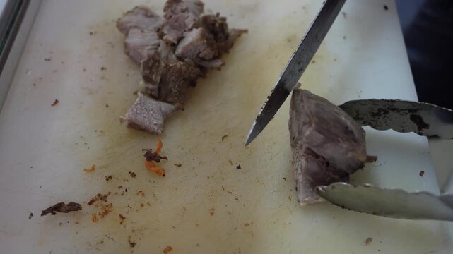Close-up 4K footage of chef hand cutting slicing boiled beef meat on white plastic cutting board using knife and tongs.
