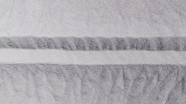 Parallel Lines Being Etched Into Fine Grey Sand Surface