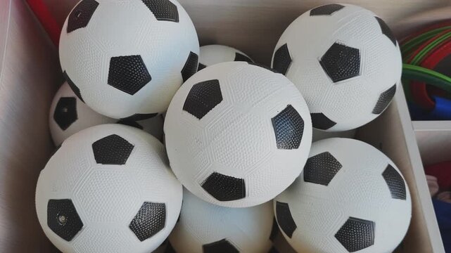 Multiple classic black and white toy soccer balls piled in a wooden box. Sports equipment for sale in a store for playing football