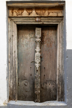 Weathered wooden door with a carved central post and aged timber lintel set in a whitewashed and grey painted wall with a small number plate, Stone Town, Tanzania