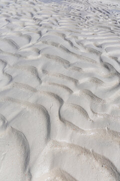 Wet white sand sculpted into soft flowing ripple patterns by the retreating tide with gentle shadows creating texture across the whole frame on a sunny day, Jambiani, Tanzania