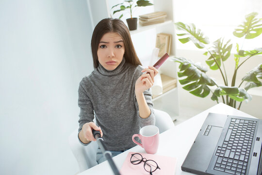Sad and dissapointed blogger is sitting in a bright room and looking to the camera. She is upset. Girl holds two small hair brushes in her hands. She is recording it on camera that is on selfie-stick.