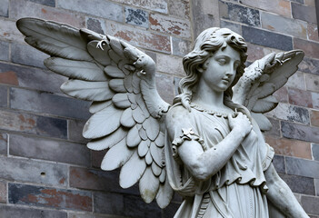 Fototapeta premium Spirituality and mourning, stone angel statue with wings against a brick wall for funeral services, religious faith and afterlife memorial