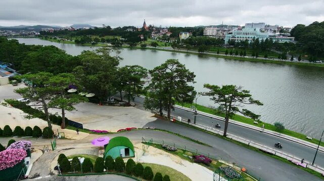 Aerial view of serene lake with lush greenery and distant town under overcast sky