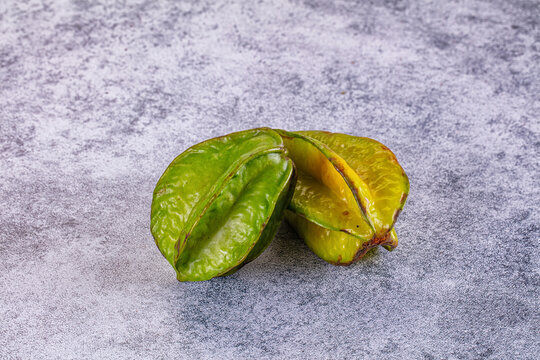 Two star shaped green and yellow carambola fruits resting on textured gray surface, tropical fruit