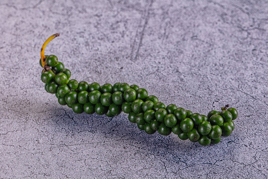 Green peppercorns on curved stem against textured gray surface, spice ingredient