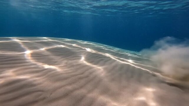 Sunlight rays illuminating mesmerizing ripple patterns on a sandy ocean seabed with moving sediment