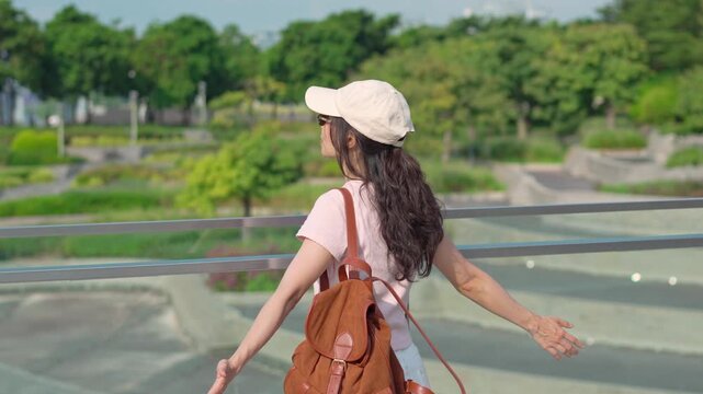 Back view of female tourist walking along the walkway enjoying freedom in green city park