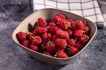 Fruit bowl containing ripe red raspberries on grey textured surface with checkered cloth, berry snack © Andrei Starostin
