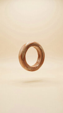 Brown textured donut shape floating against a matching neutral beige background with textured floating background levitation suspension minimalist lighting vertical composition circular