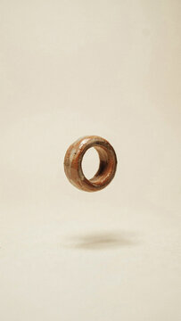Small wooden ring floating above a textured beige surface with floating geometric accessory ornament composition abstract background material sculpture component isolated photography