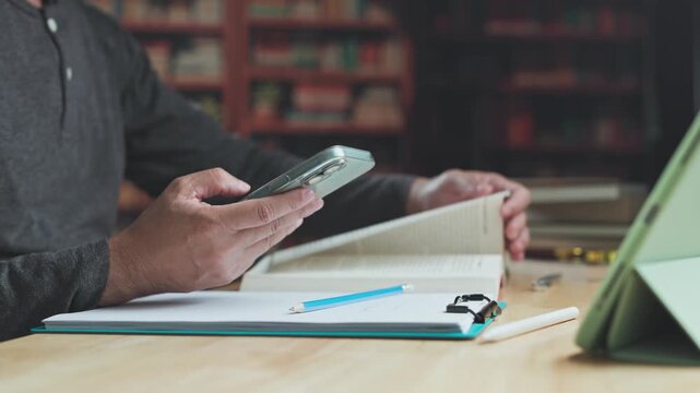 Researcher conducts research across mobile devices, continuing digital research beside study notes textbook materials.