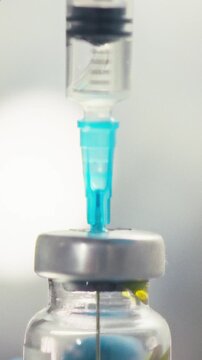 Medical professional wearing protective nitrile gloves inserts syringe needle into sealed glass medicine bottle inside hospital, managing dosage preparation for pharmacology and healthcare procedures