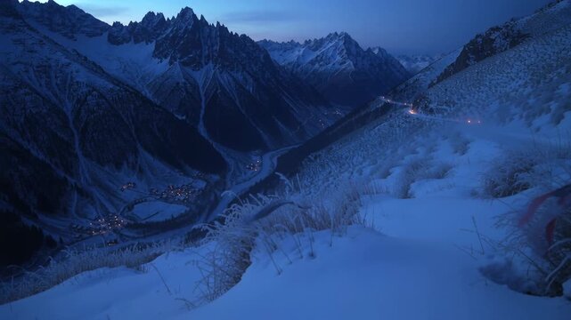 Panning camera over snow hummock on ridge as dawning, revealing valley lights, ribbon fluttering