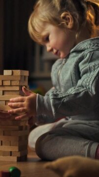 Mother and young daughter sit together on the floor during early evening, playing a game of balance with wooden blocks, building a tower - concept of family, childhood, and interactive parenting