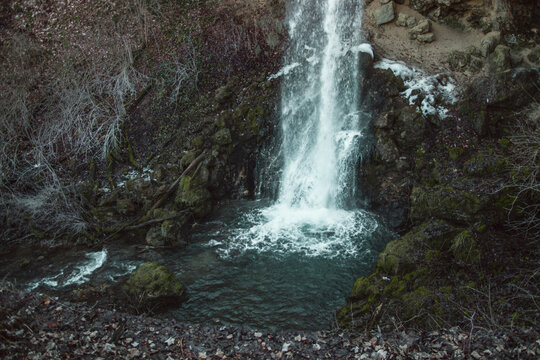 hungary, miskolc 2021 02 04: Winter waterfall flowing over mossy rocks into a pool, natural daylight, vertical shot.