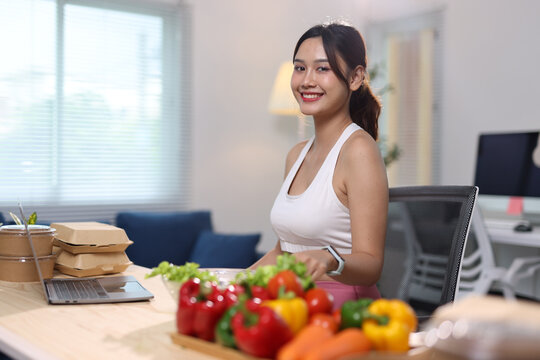Young woman smiling while preparing a healthy vegetable salad at her home office, focusing on wellness and nutritious eating.