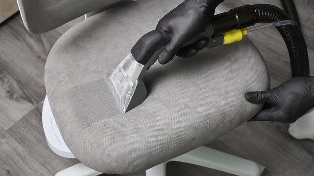 Worker deep cleans gray chair seat with extractor nozzle, creating clean strips across upholstery.