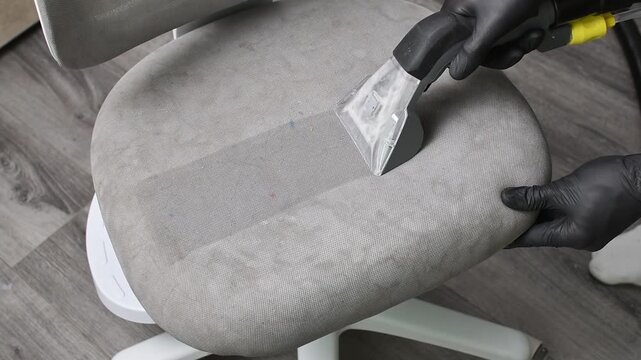 Worker uses extractor nozzle on gray chair seat to deep clean upholstery and remove embedded dirt.