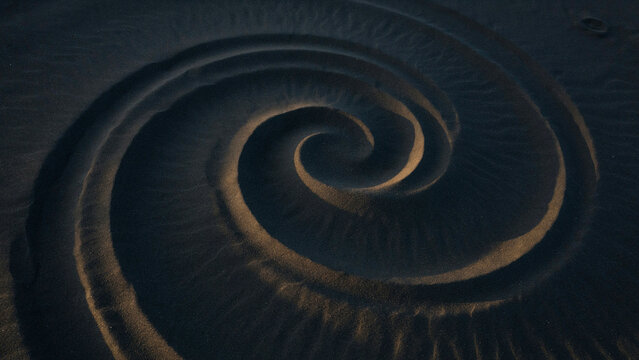 Spiral pattern raked into dark volcanic sand with volcanic minimalist meditation meditative artistic geometry mindfulness tranquility sculpture abstract close-up sandscape simplicity
