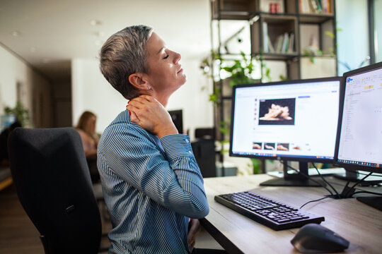 Woman rubbing sore neck at computer desk in office