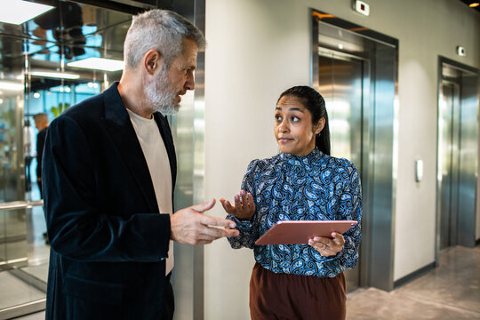 Coworkers discuss by office elevators with a tablet