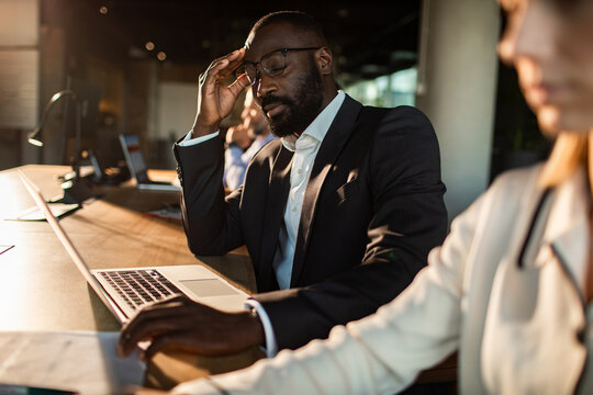 Stressed businessman holding forehead at laptop in office