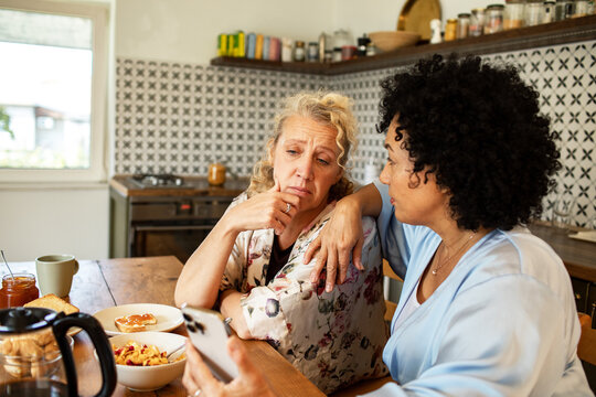 Woman comforting friend while looking at phone at kitchen table