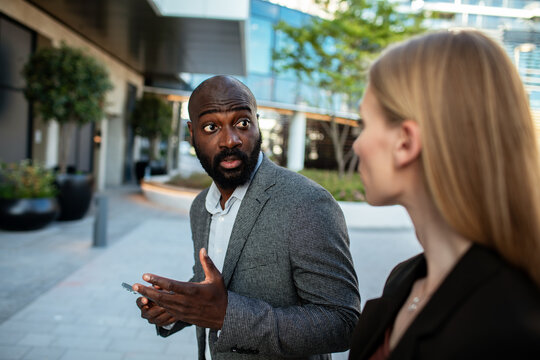 Businessman with smartphone reacting to colleague outdoors
