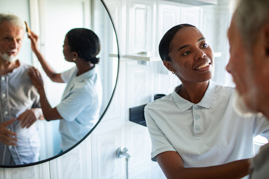 Caregiver combing elderly man's hair in bathroom